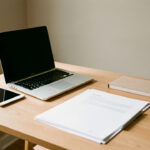 Bureau moderne de petite entreprise avec ordinateur portable, tablette, documents vierges et agenda, éclairé par la lumière naturelle.