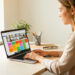Une femme freelance travaille à domicile sur un ordinateur portable posé sur un bureau lumineux, avec une visioconférence et un tableur visibles à l’écran dans une ambiance professionnelle.